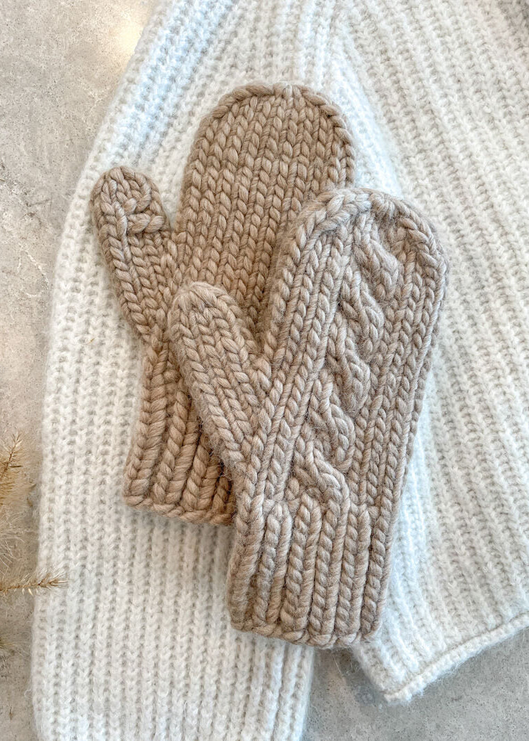 Pair of beige knitted mittens on a textured surface