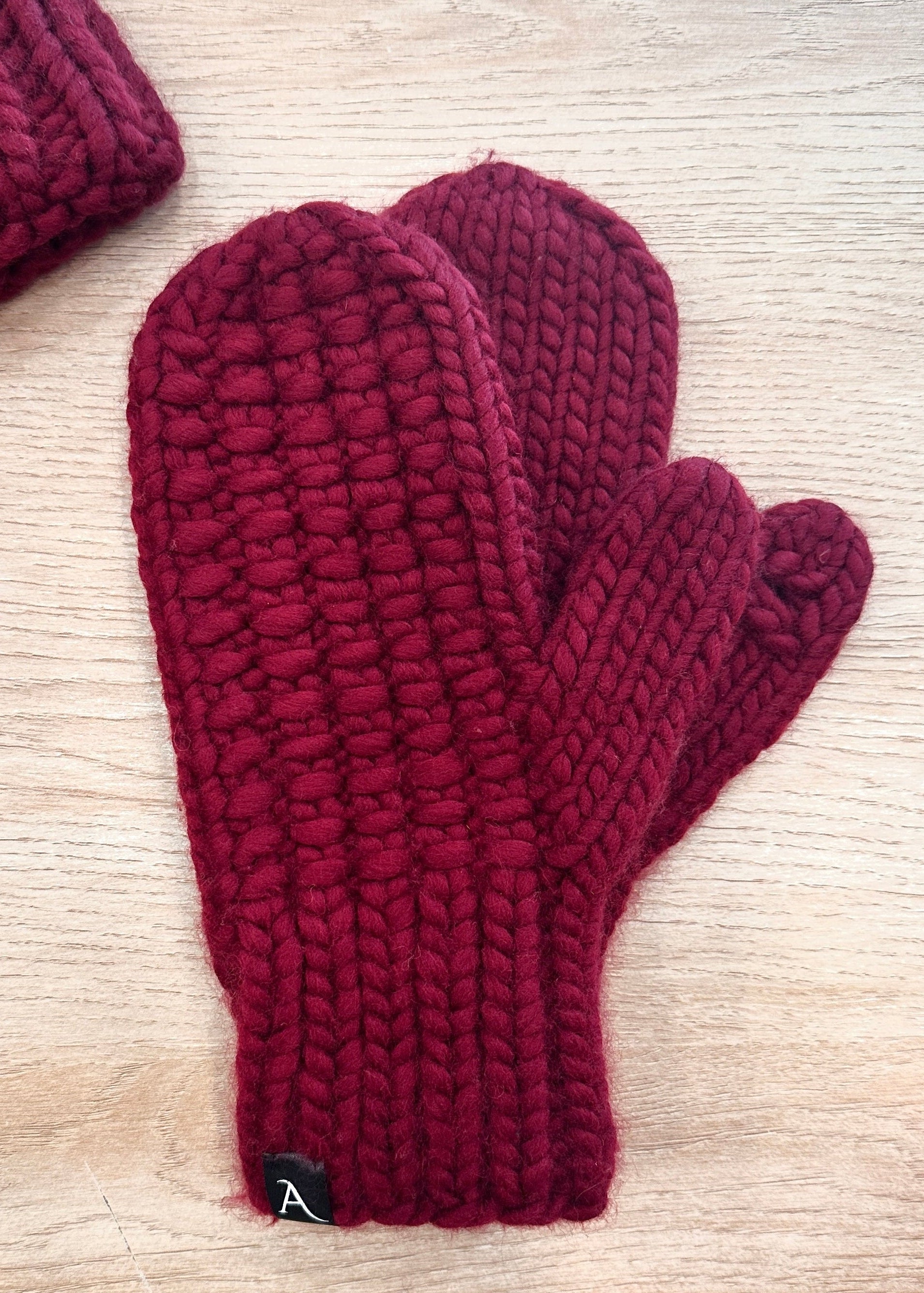 Pair of maroon knitted mittens on a light wooden surface