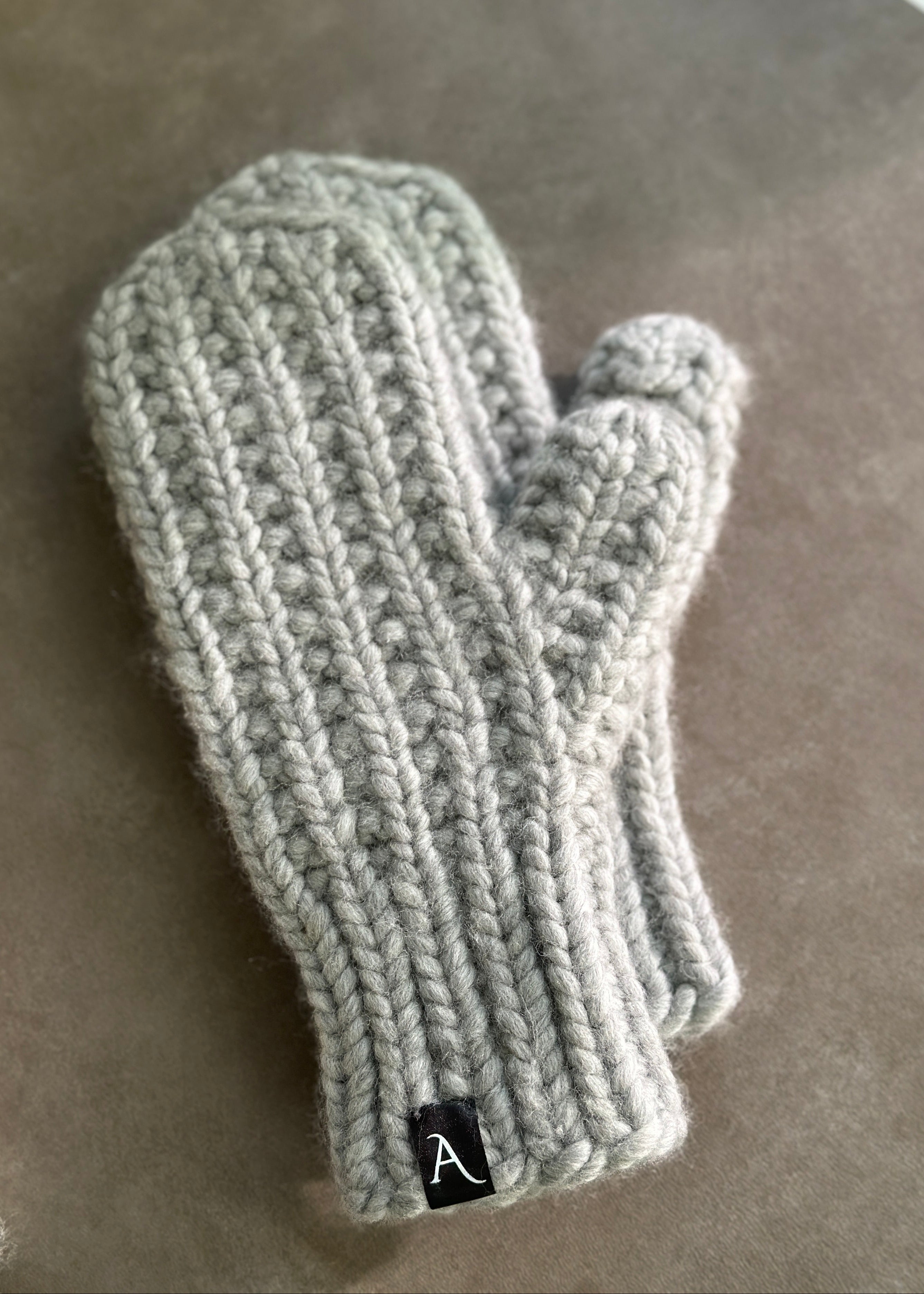 Knitted gray mitten with a brand label on a brown surface