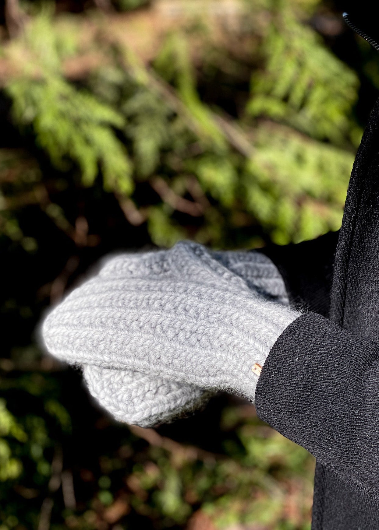 Close-up of a person wearing gray gloves with a blurred green forest background