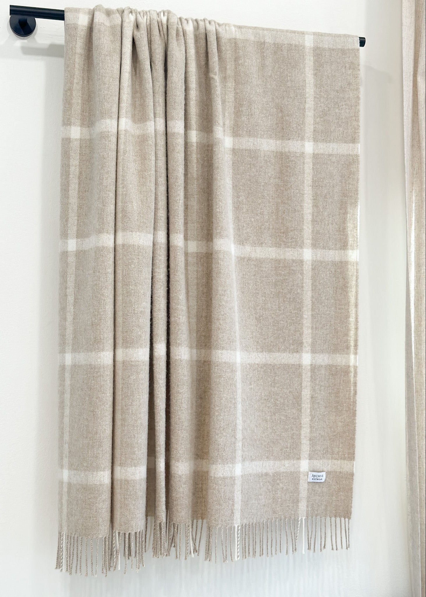 Plaid blanket with fringes hanging on a rod against a white background