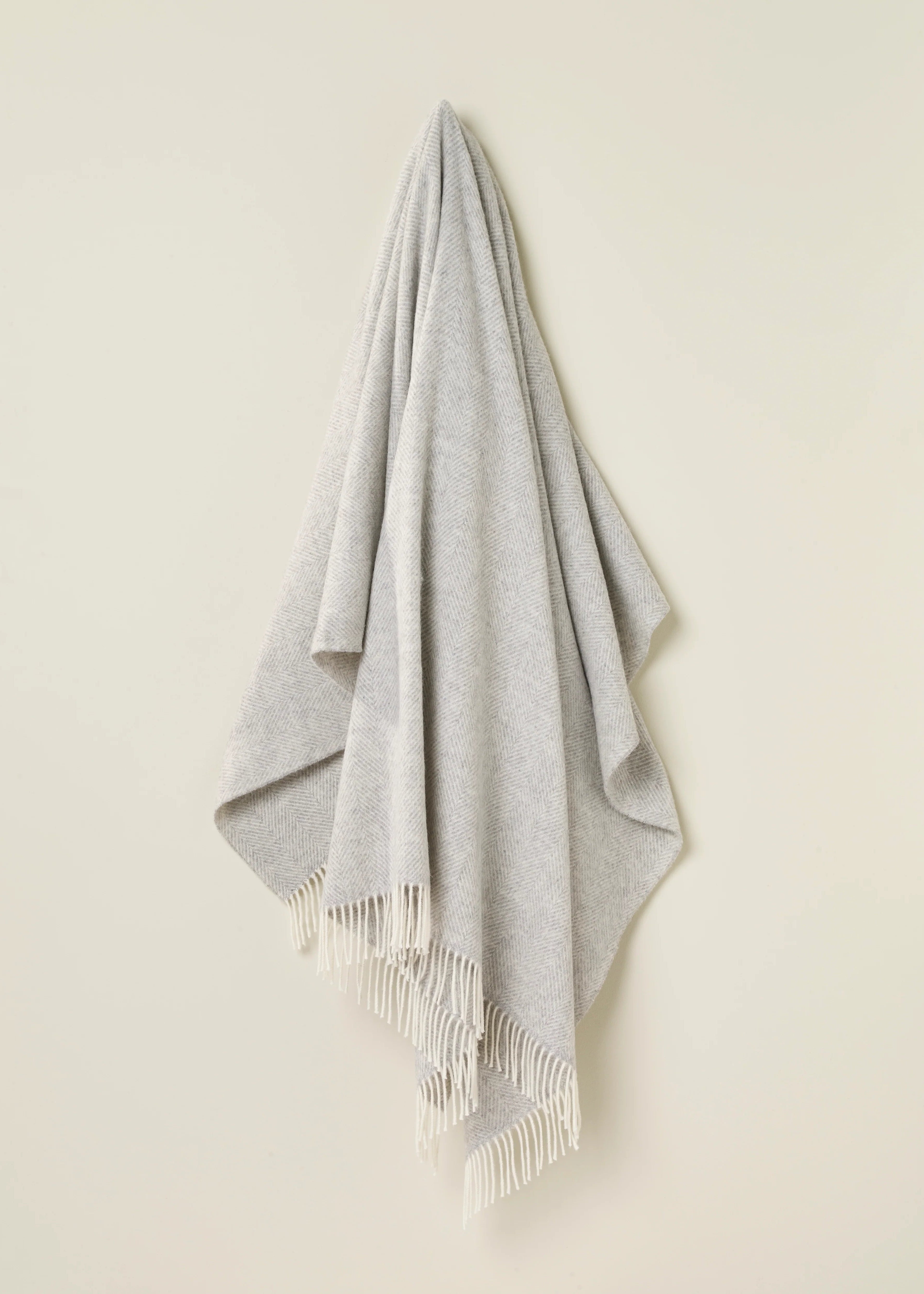 Gray throw blanket with fringe hanging on a neutral background