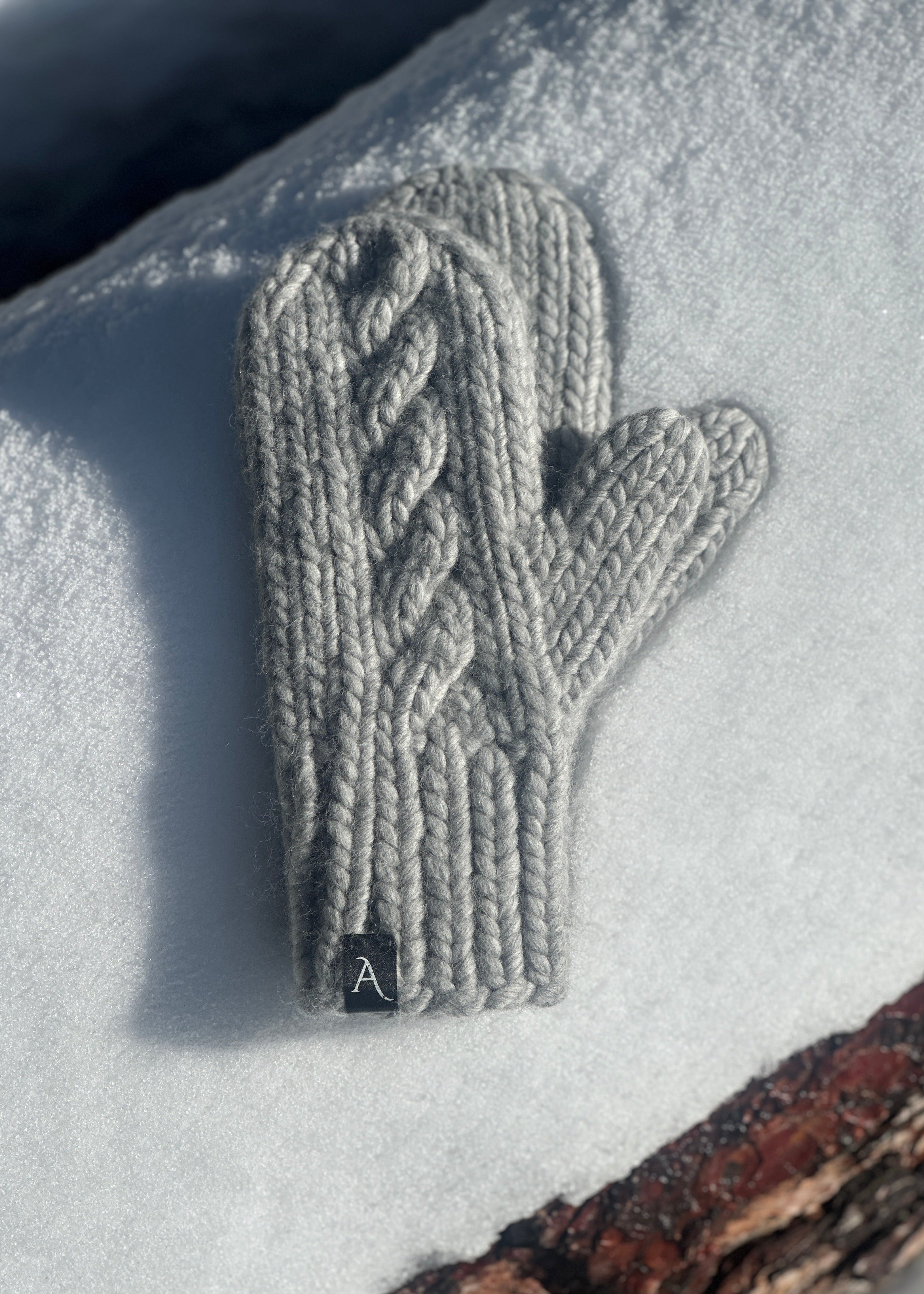 Knitted gray mittens with cable knit pattern on a snowy surface