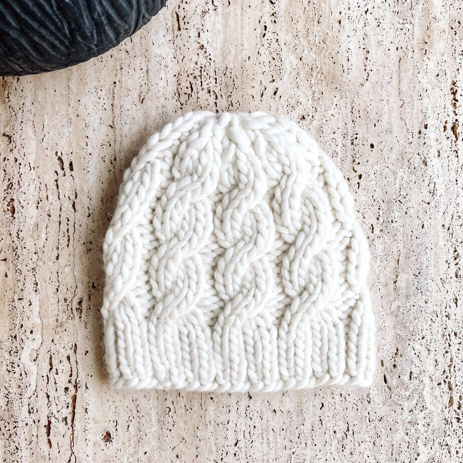 Ivory cable knit beanie hat on a textured surface