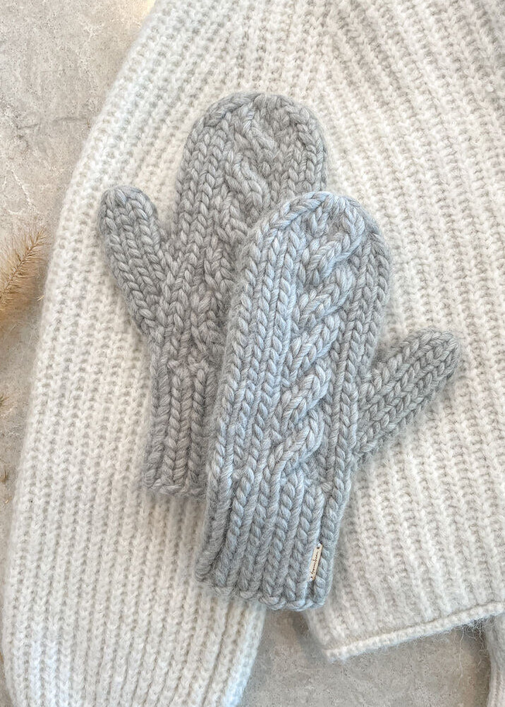 Pair of gray knitted mittens on a textured surface