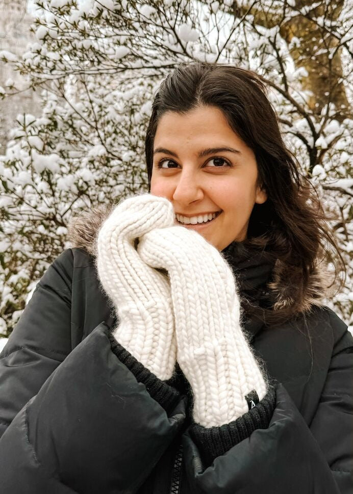 Woman wearing white knitted mittens in a snowy outdoor setting