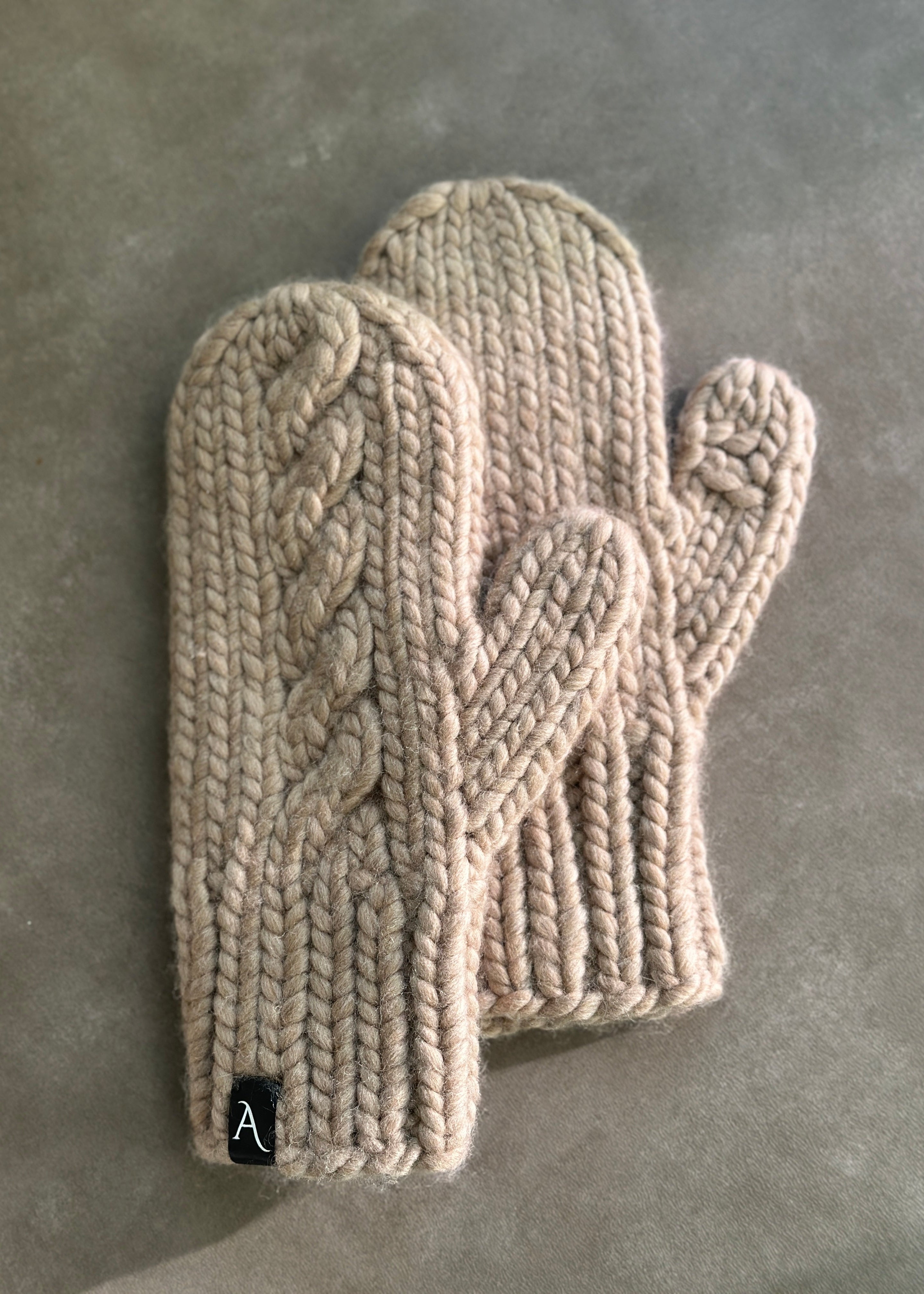 Pair of beige knitted mittens on a gray surface