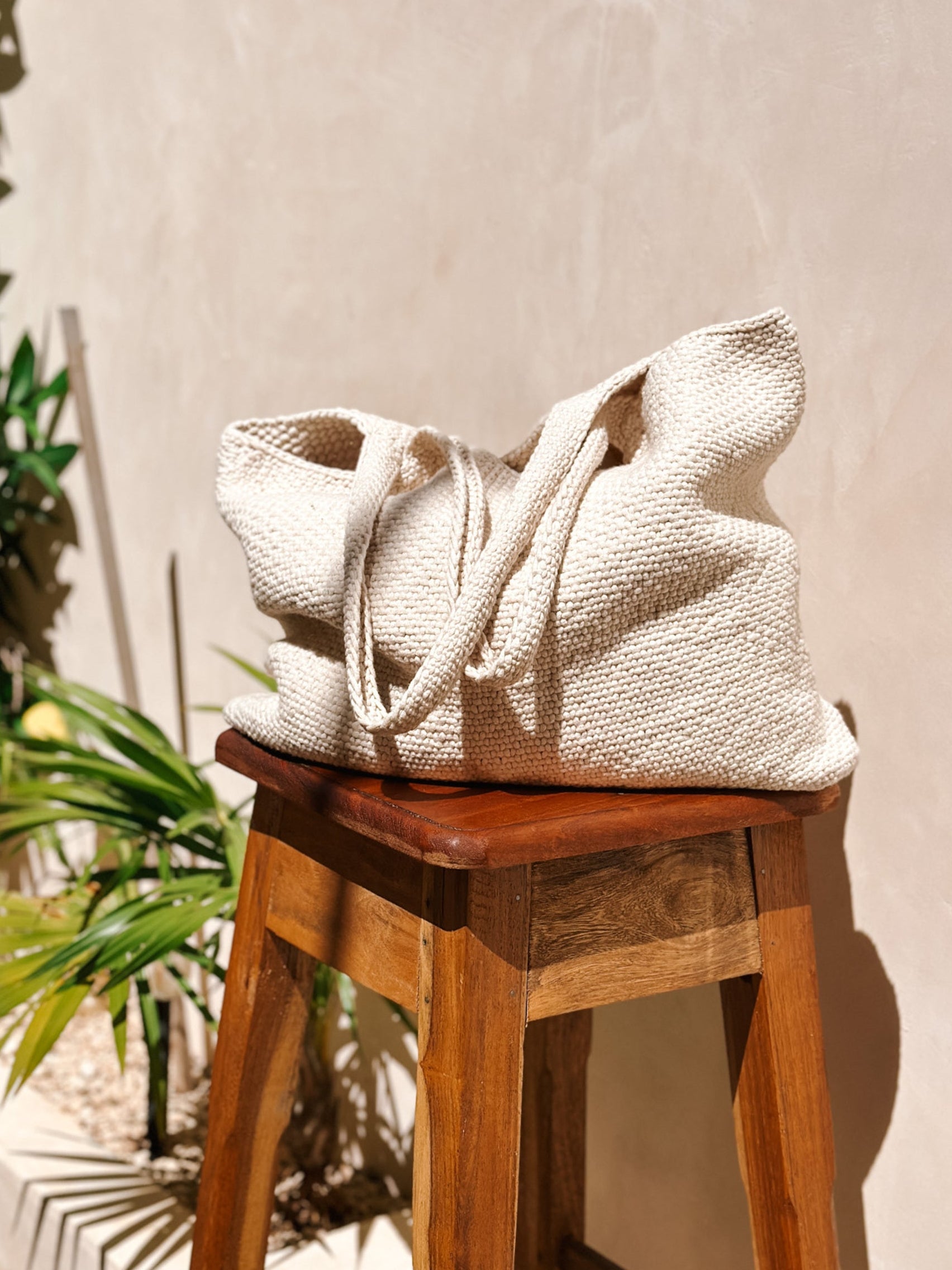 Textured Knit Ivory, off-white bag on a wooden stool with plants in the background