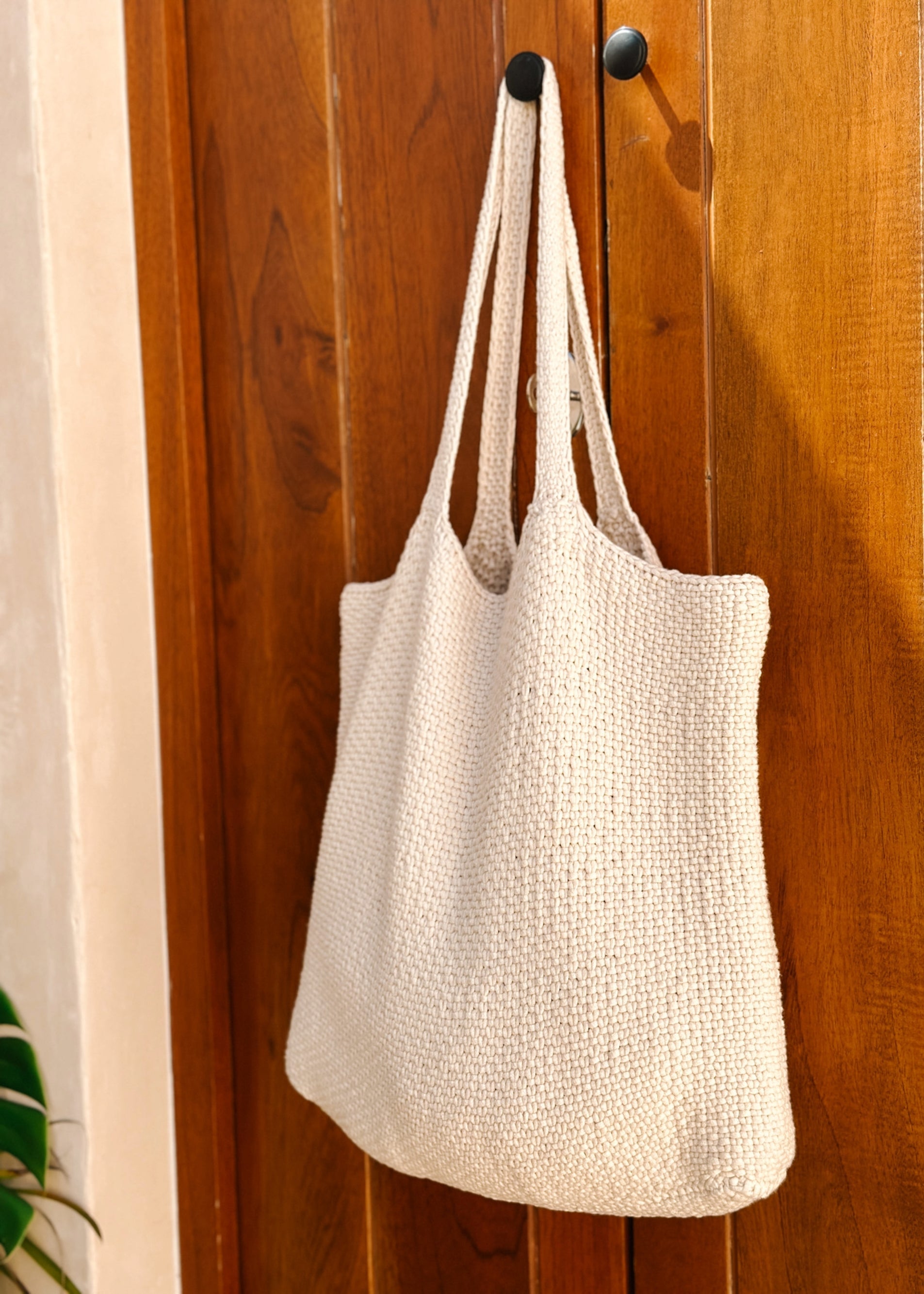 White woven tote bag hanging on a wooden door