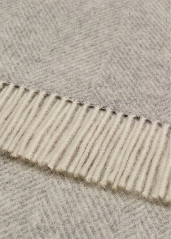 Close-up of a textured wool blanket with a herringbone pattern and fringe on the edge.