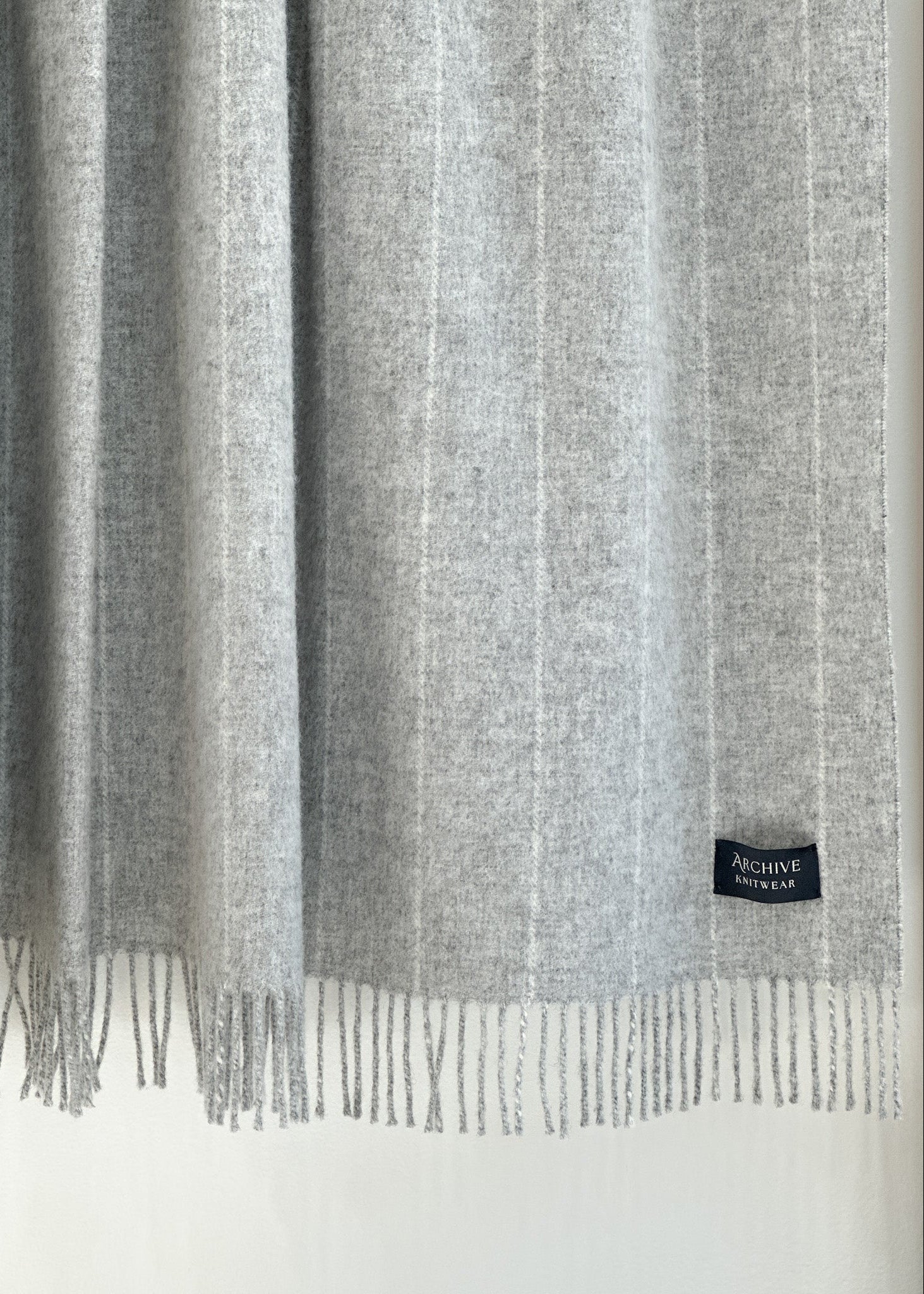 Gray scarf with fringes and a brand label on a white background