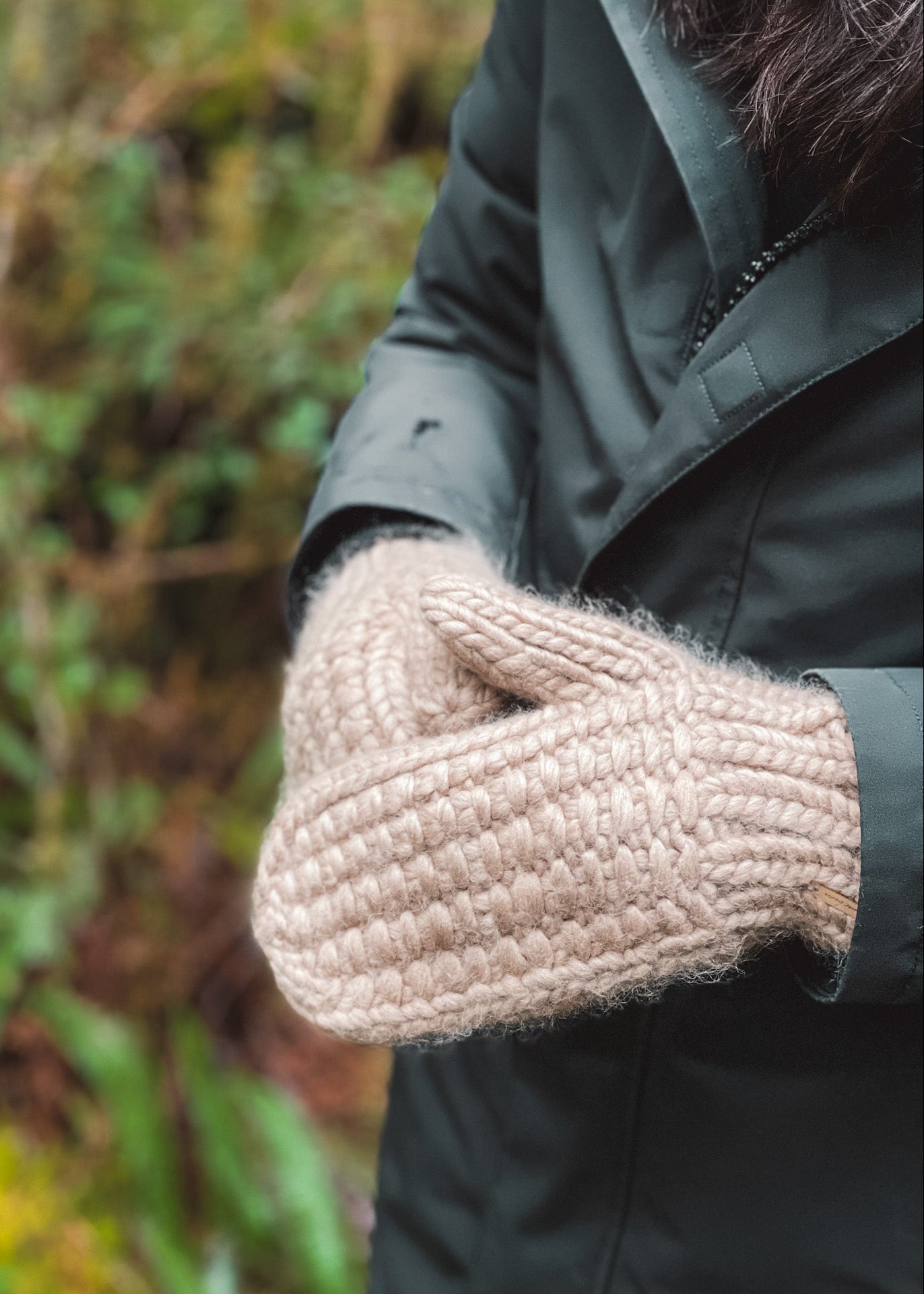 Close-up of a person wearing a dark coat with a beige knitted glove against a blurred natural background.