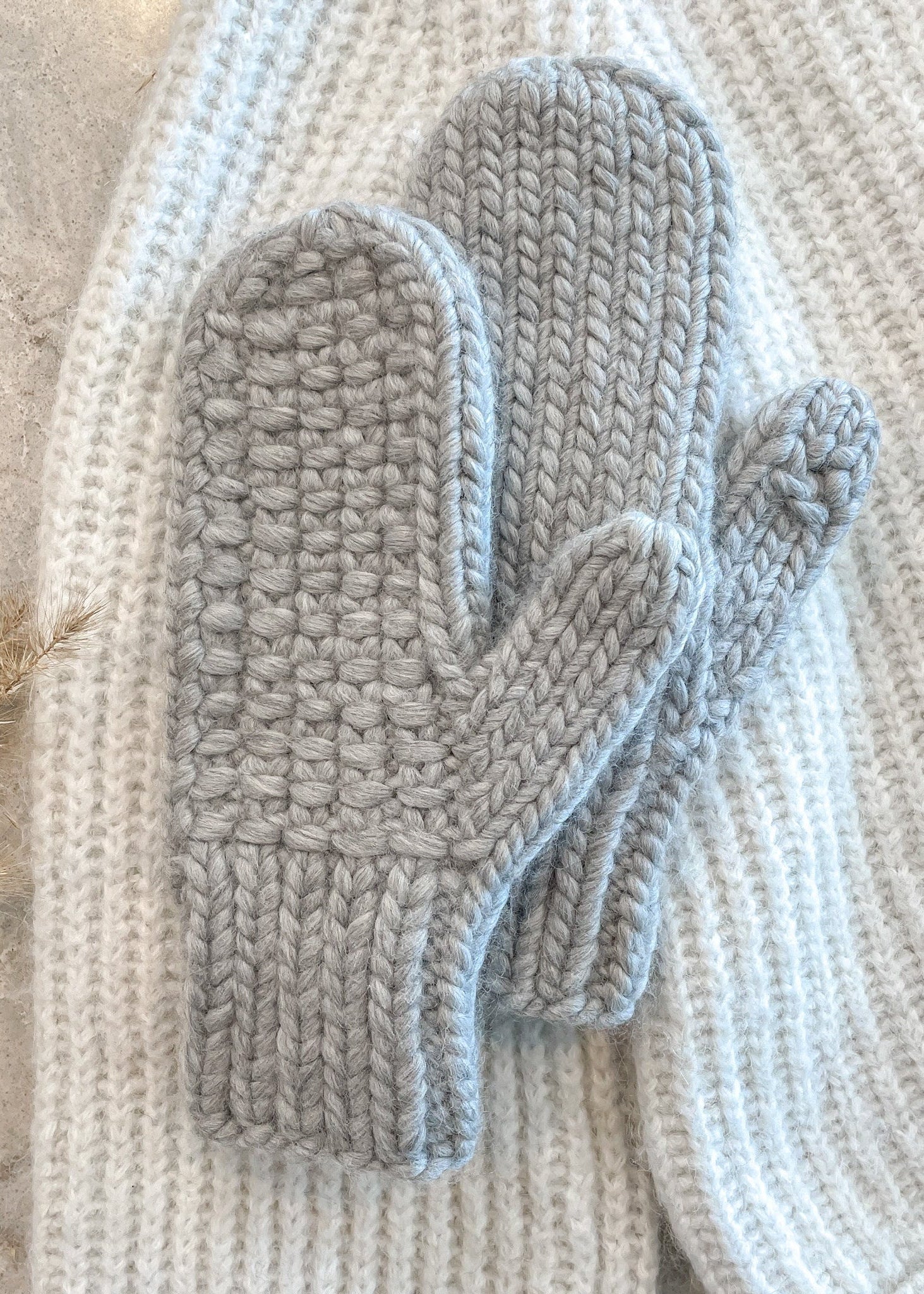 Pair of gray knitted mittens on a textured surface