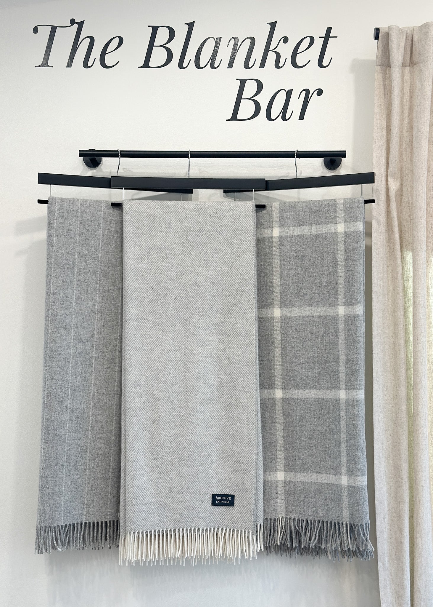three Gray blankets hanging on a rack in herringbone pattern, pinstripe pattern and plaid windowpane pattern