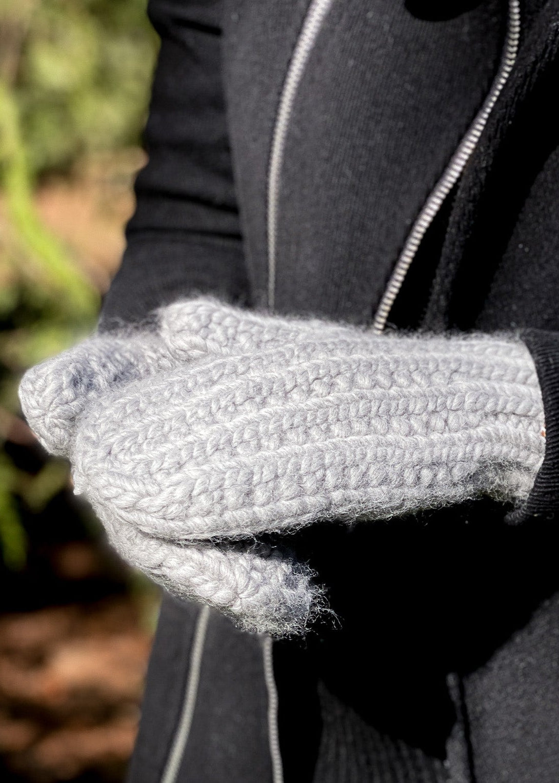 Person wearing gray knitted mittens with a blurred natural background