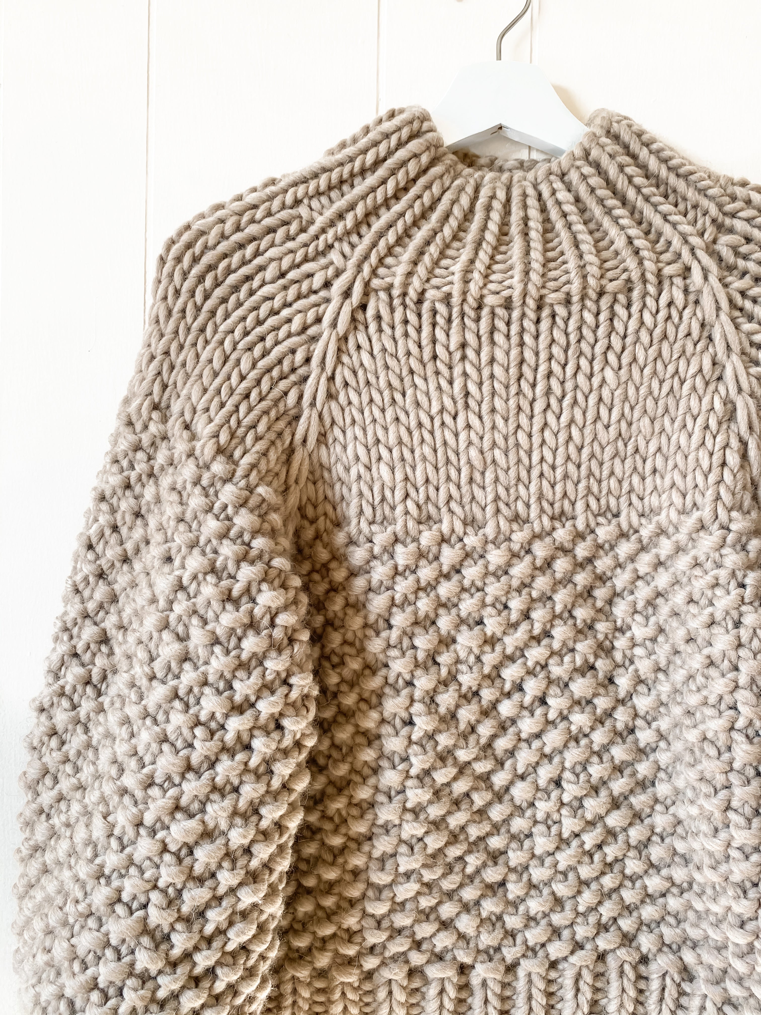 a closeup shot of a Beige chunky knitted sweater on a hanger against a white background